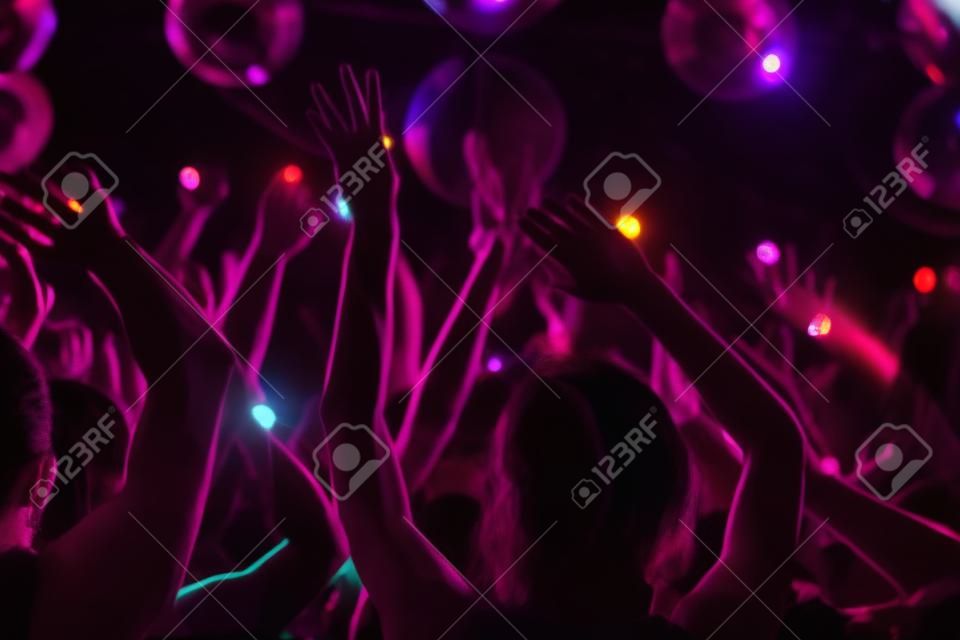 Multitud de personas con los brazos levantados bailando en club nocturno