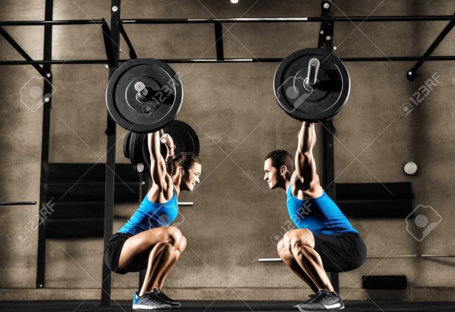 Active young man and woman lifting heavy barbells opposite one another