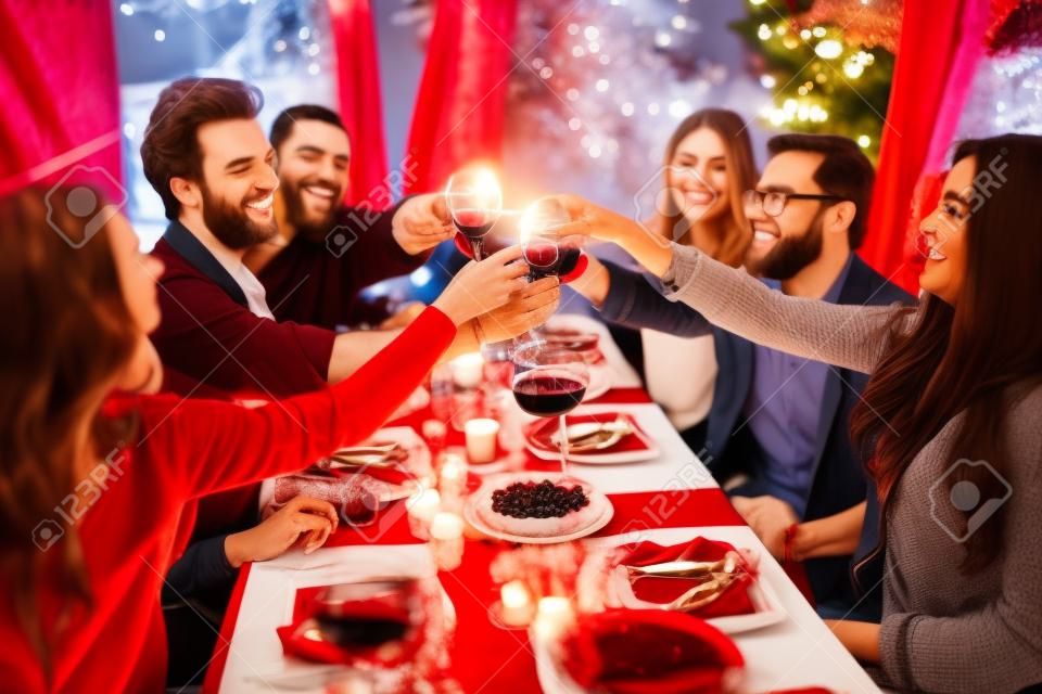 Felices amigos con copas de vino tinto tostado en mesa festiva