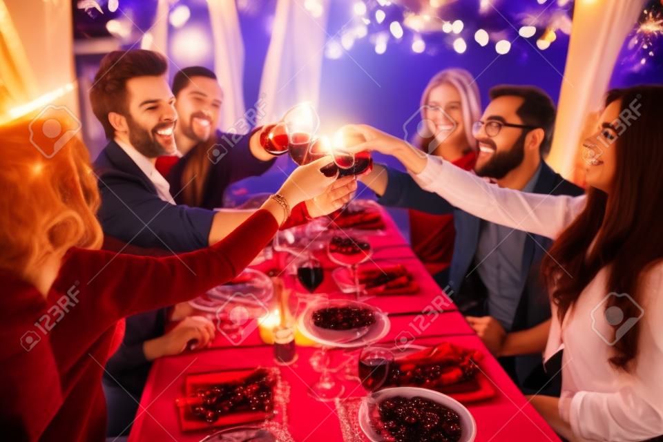 Felices amigos con copas de vino tinto tostado en mesa festiva