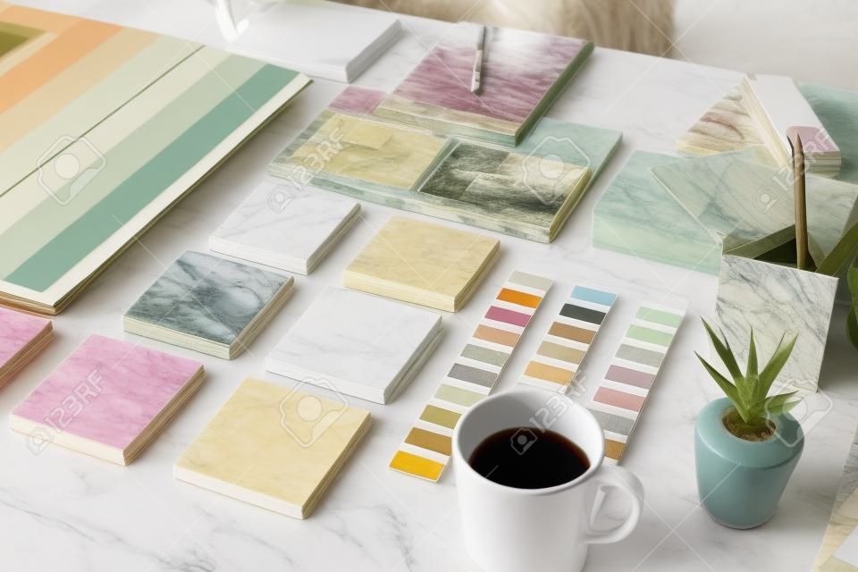 Collections de carreaux de marbre, papiers peints, échantillons de couleurs, photos de l'intérieur de la maison, tasse de thé, ensemble de papiers à lettres et plantes domestiques sur le bureau