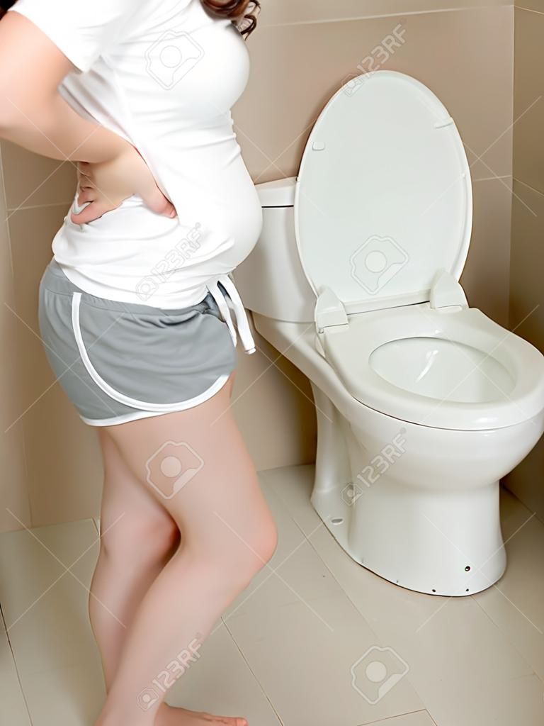 schönes süßes Mädchen, das auf dringendem Entfernen des Badezimmers steht Hosen, weil sie Magenschmerzen glaubt, Durchfall nach dem Essen zu essen.