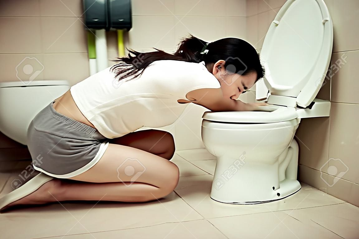 young beauty woman drunk feeling stomach uncomfortable and kneeling in front of bathroom toilet vomiting after party time.