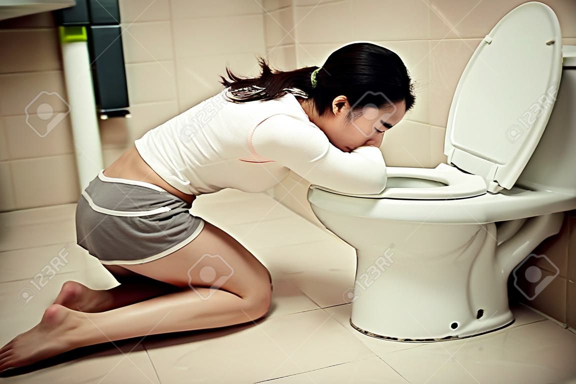 young beauty woman drunk feeling stomach uncomfortable and kneeling in front of bathroom toilet vomiting after party time.