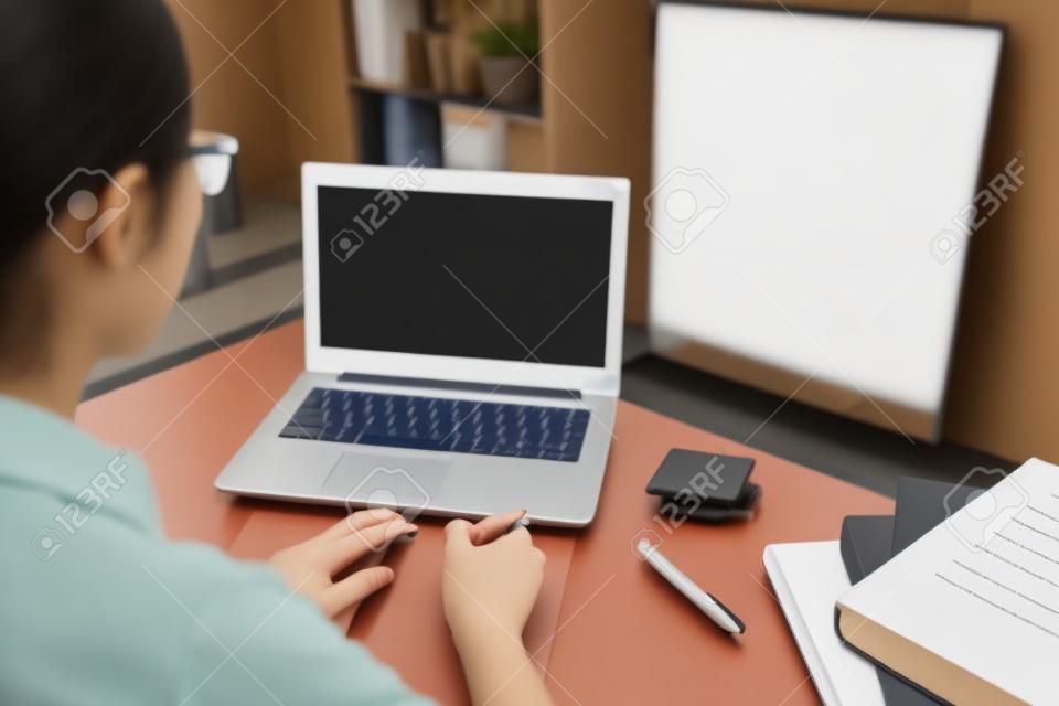 hintere Ansicht des weiblichen Hochschulstudenten, der den mobilen Laptop studiert durch on-line-E-Learning-System mit weißem leerem Bildschirm verwendet. Foto des vorgewählten Fokus.