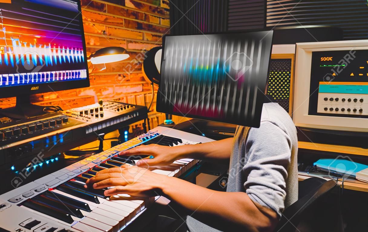 young asian male composer playing midi keyboard for arranging a song on computer in home studio