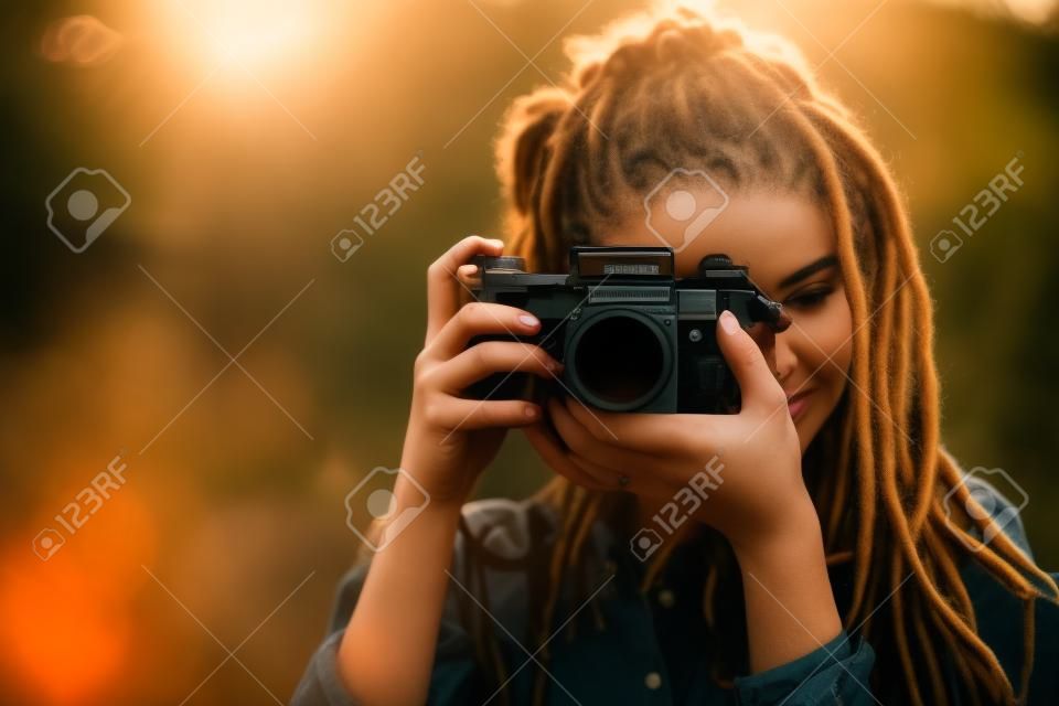 Hipster atrakcyjna fotografia dziewczyna z dredami strzelająca do natury w zachodzie słońca w lesie, widok na zewnątrz