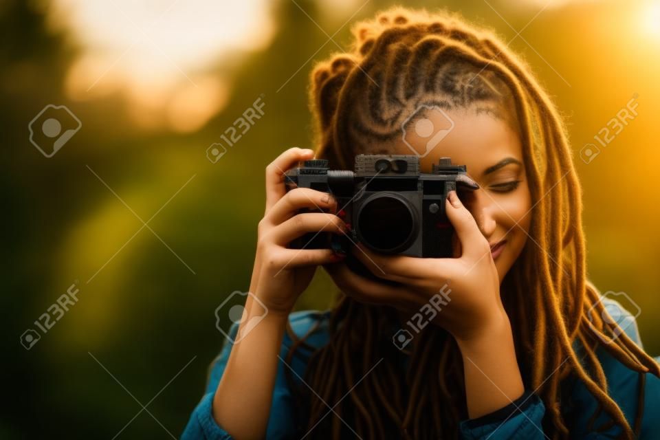 Menina de fotografia atraente hipster com dreads tiro na localização da natureza no pôr do sol na floresta, vista ao ar livre