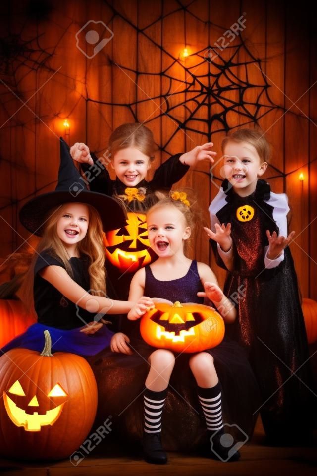 Crianças alegres em trajes de halloween comemorando o dia das bruxas em um celeiro de madeira com abóboras. Conceito de dia das bruxas.