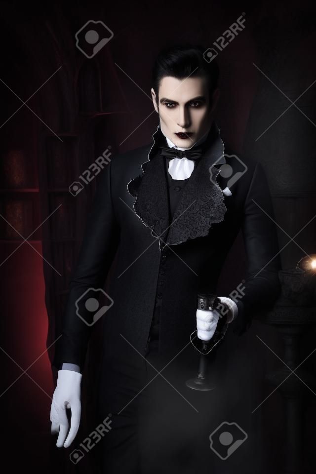 Handsome vampire man wearing elegant tailcoat stands in the old medieval castle. Halloween.