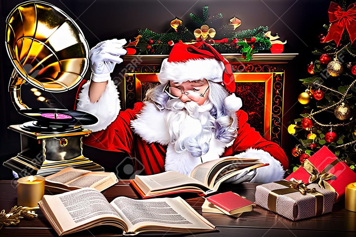 Il buon vecchio Babbo Natale a leggere un libro e ascoltando vecchio grammofono a casa. Canzoni di Natale. Concetto di Natale.