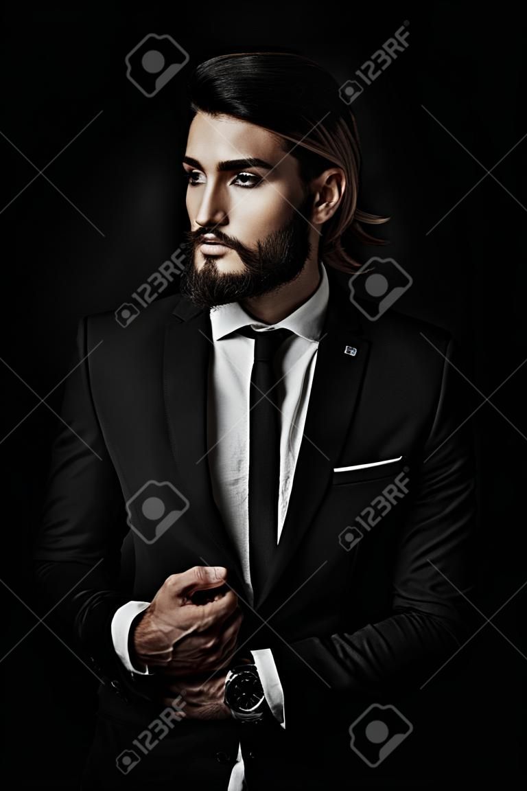 Disparo de moda. Hombre joven hermoso que presenta en traje elegante y camisa blanca sobre fondo negro. Belleza masculina, moda.