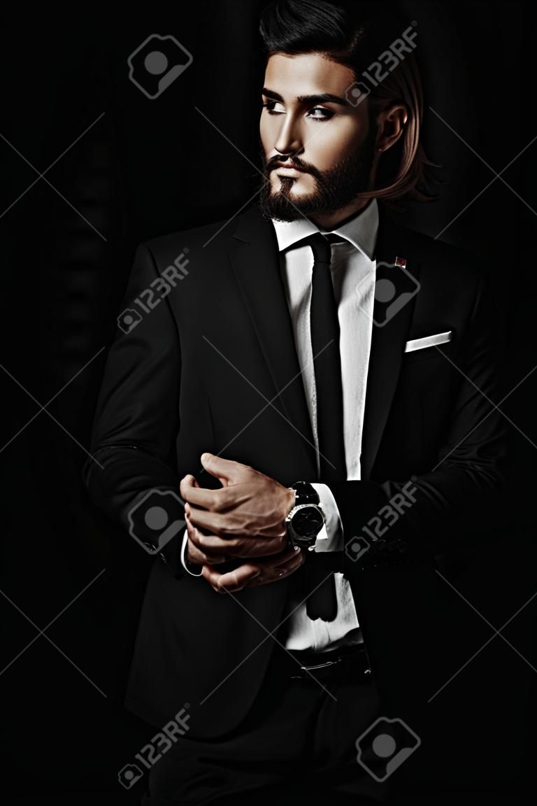 Fashion shot. Handsome young man posing in elegant suit and white shirt over black background. Men's beauty, fashion.