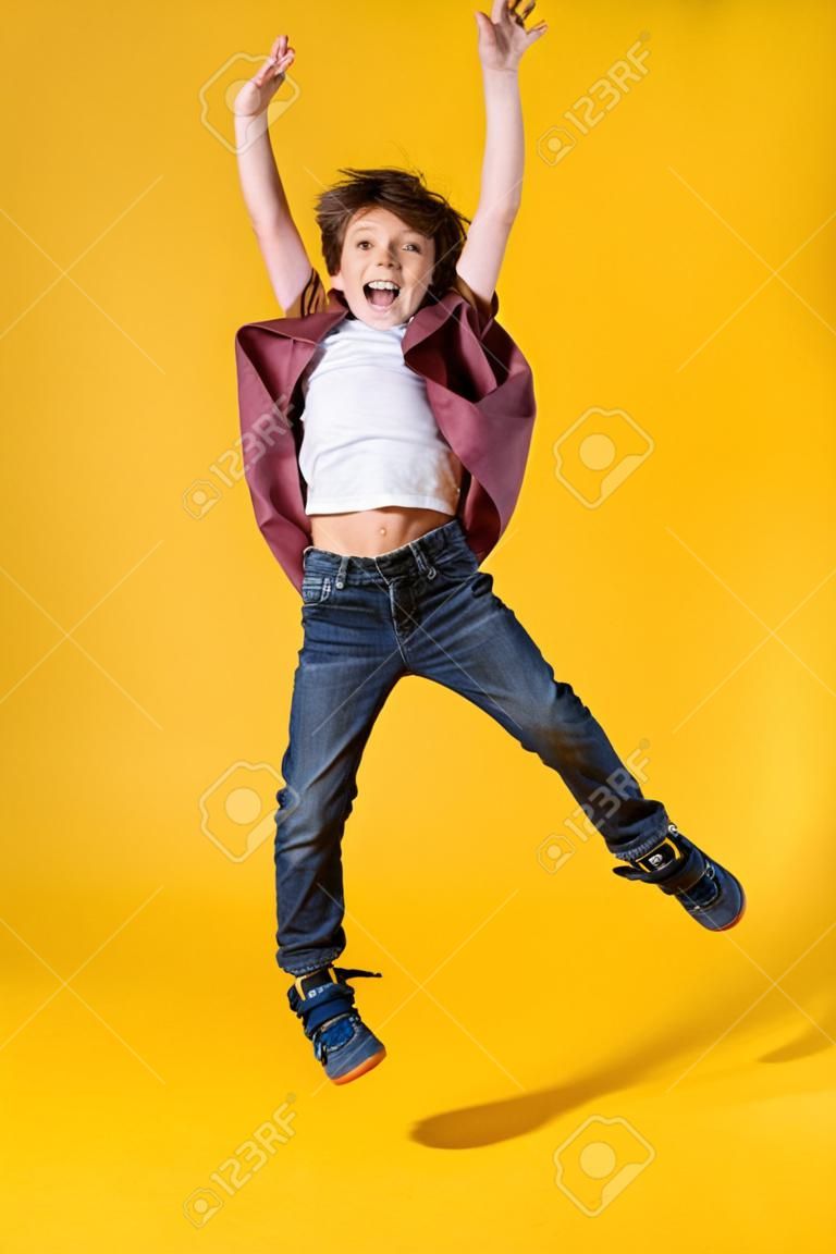 A full length portrait of a bright young boy jumping in the studio over the yellow background. Kids, fashion.