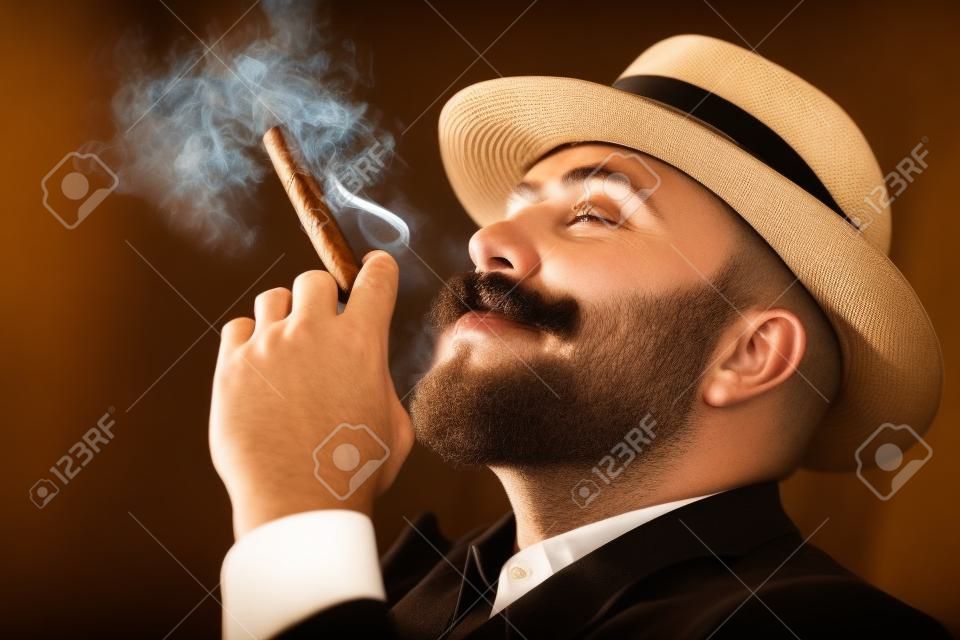 A close up portrait of a thoughtful man with a cigar posing in the vintage interior. Men's beauty, fashion, style.