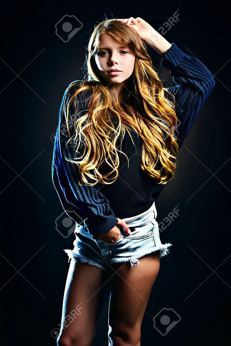 A portrait of a pretty fashionable girl posing over the black background. Fashion for teenagers, beauty.