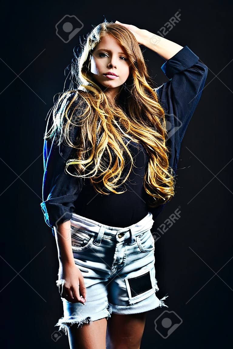 A portrait of a pretty fashionable girl posing over the black background. Fashion for teenagers, beauty.