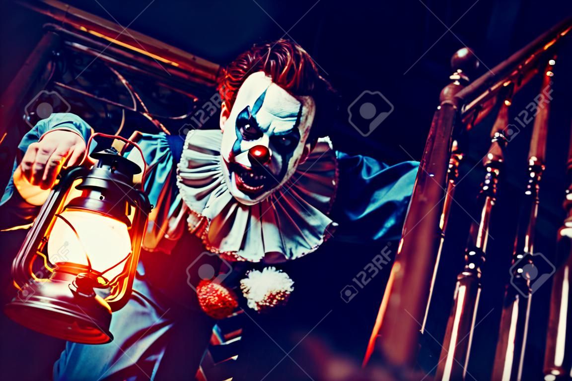 Portret wściekłego szalonego klauna z horroru z latarnią na schodach. Halloween, karnawał.