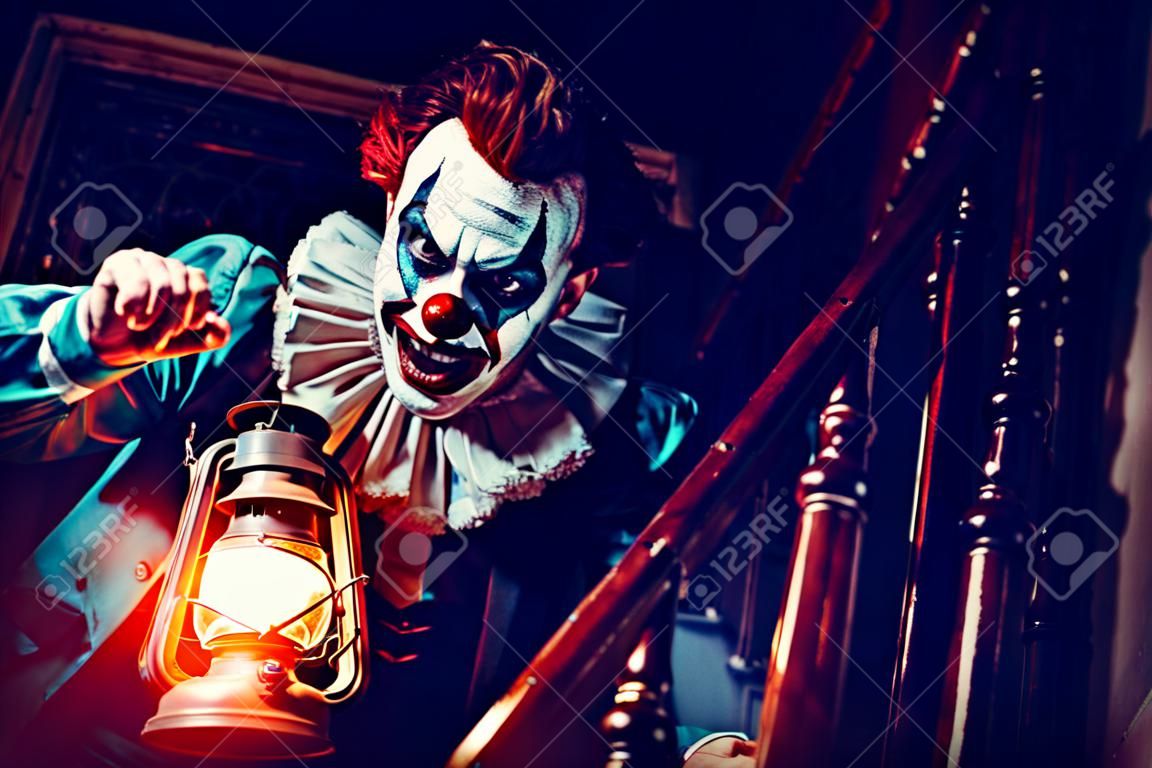 Un portrait d'un clown fou en colère d'un film d'horreur avec une lanterne dans les escaliers. Halloween, carnaval.