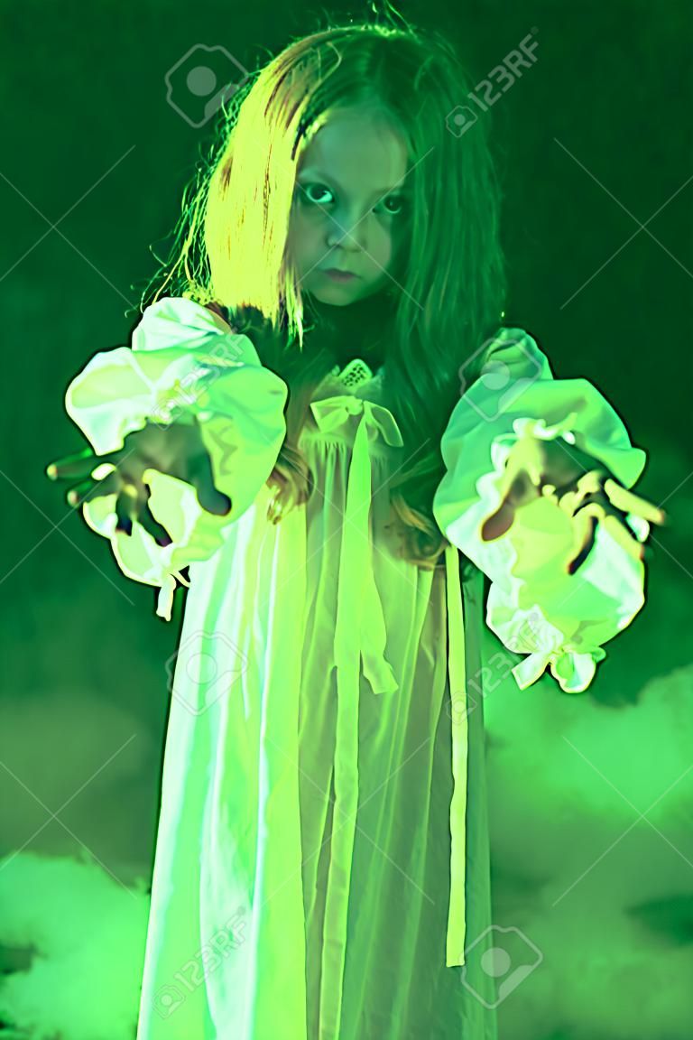 Scary little girl ghost in a white nightgown holds out her hands forward. Black background. Halloween.