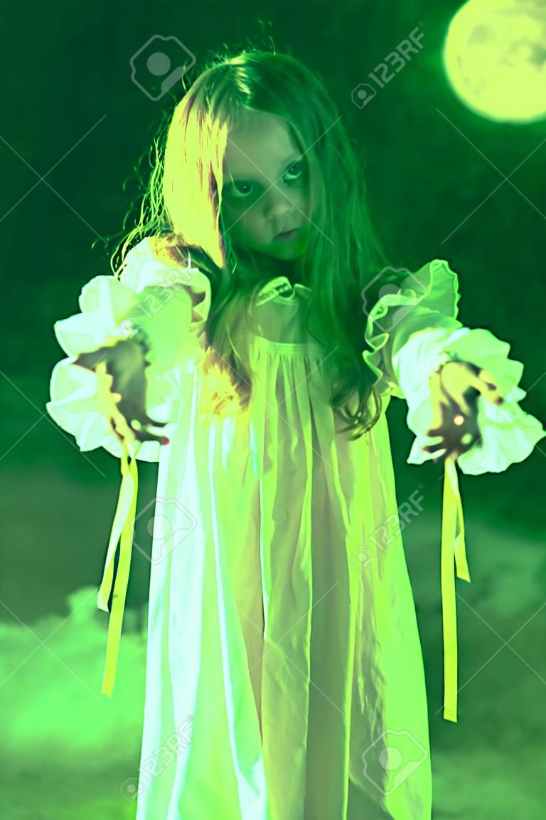 Scary little girl ghost in a white nightgown holds out her hands forward. Black background. Halloween.