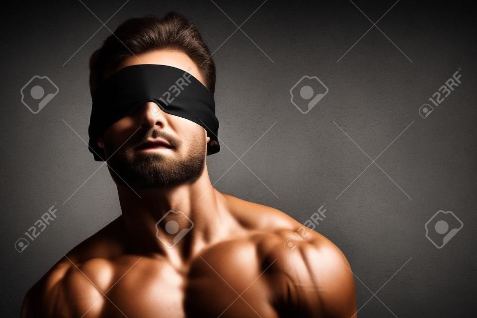 Retrato de arte de un apuesto joven atlético con los ojos vendados con cuerpo musculoso perfecto. Deportes y musculación. Belleza y salud masculina. Copie el espacio.