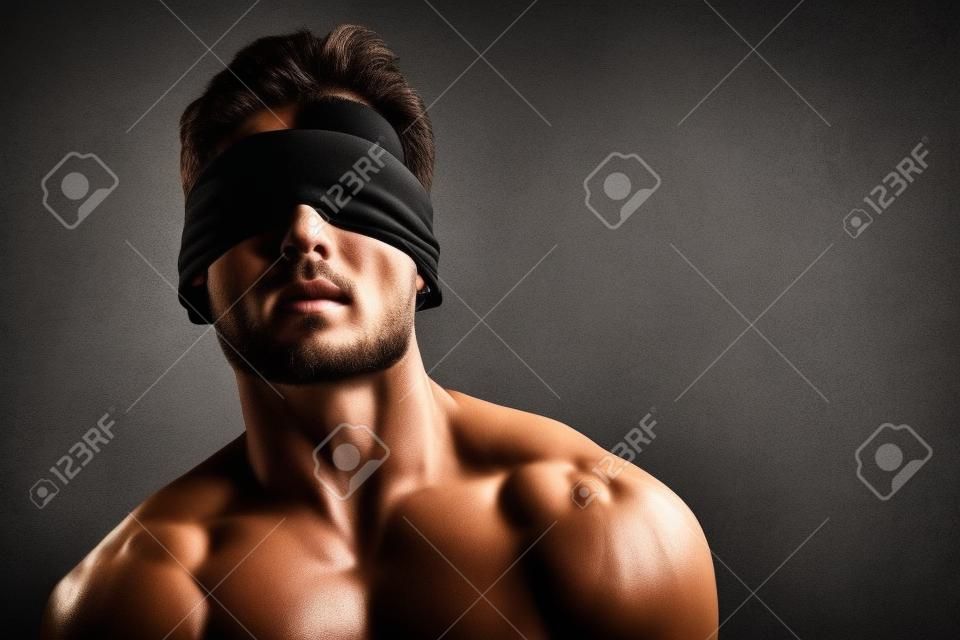 Retrato de arte de un apuesto joven atlético con los ojos vendados con cuerpo musculoso perfecto. Deportes y musculación. Belleza y salud masculina. Copie el espacio.