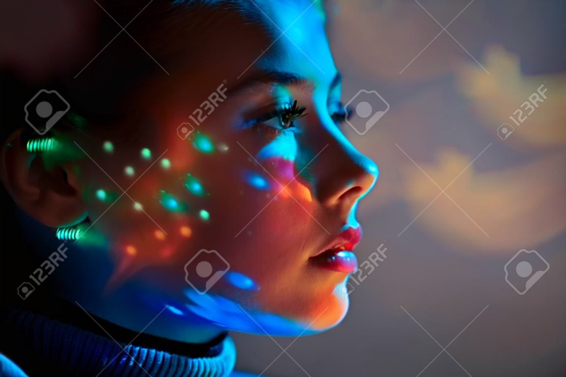 Close up portrait of beautiful tender girl looks into the distance with colored lights on your face against the background of outer space. Space concept.