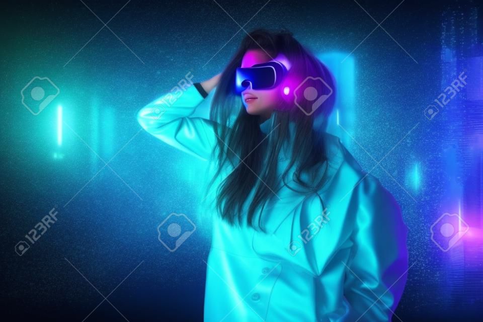 Virtual reality, city of the future. Beautiful cyber girl in hi-tech clothes of the future stands in the neon light of the night cyber city in the rain.