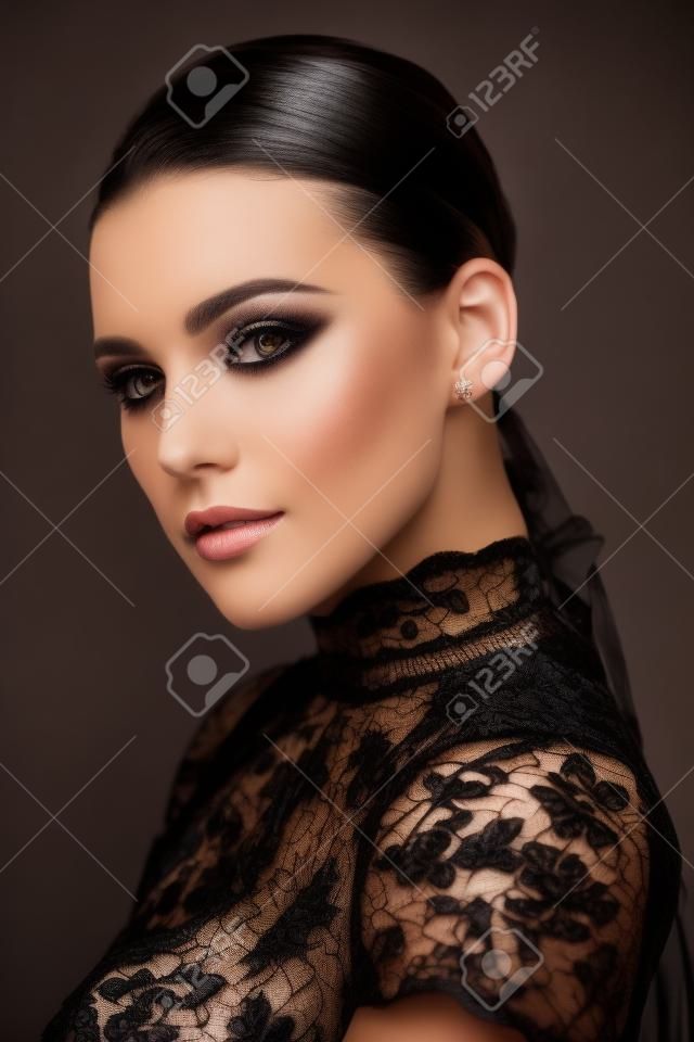 Portret van een mooie brunette vrouw mode model met elegante make-up poseren in een zwarte kant jurk op een zwarte achtergrond. Studio portret. Mode shot.