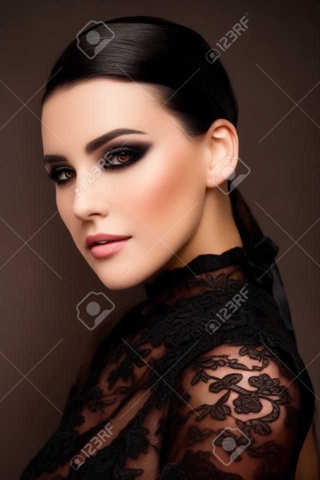 Portret van een mooie brunette vrouw mode model met elegante make-up poseren in een zwarte kant jurk op een zwarte achtergrond. Studio portret. Mode shot.