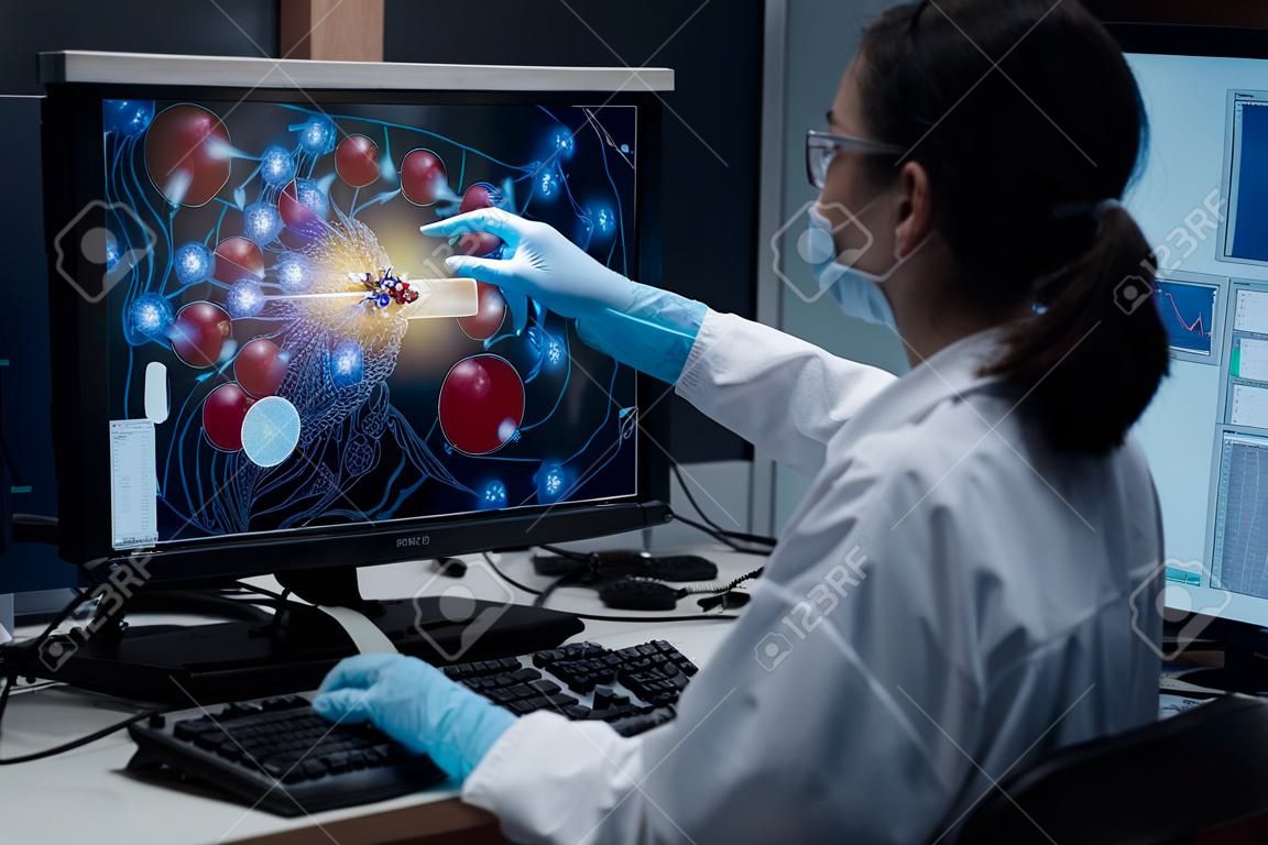 Une chercheuse indique la position de l'échantillon de médicament dans la simulation de modélisation du développement de médicaments, comme indiqué sur un écran d'ordinateur. L'ordinateur analytique est un superordinateur pour la simulation de médicaments.