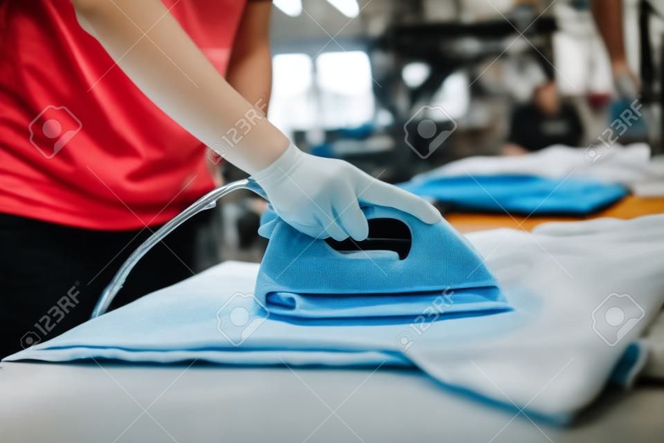 Young woman ironing waterproof film on fabric at her shop. worker working on manual screen printing on t-shirt.
