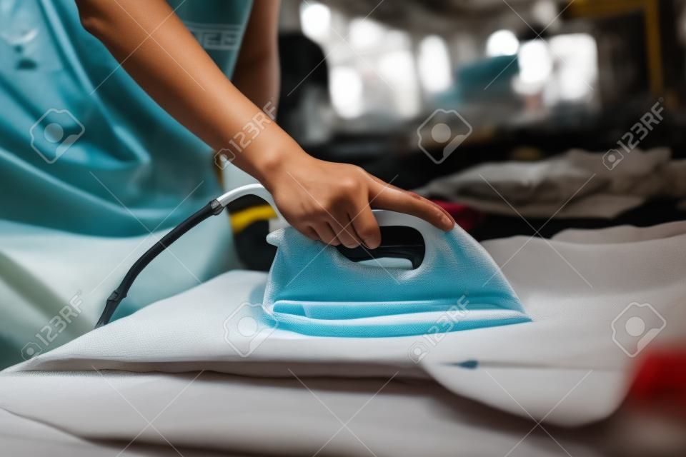 Young woman ironing waterproof film on fabric at her shop. worker working on manual screen printing on t-shirt.