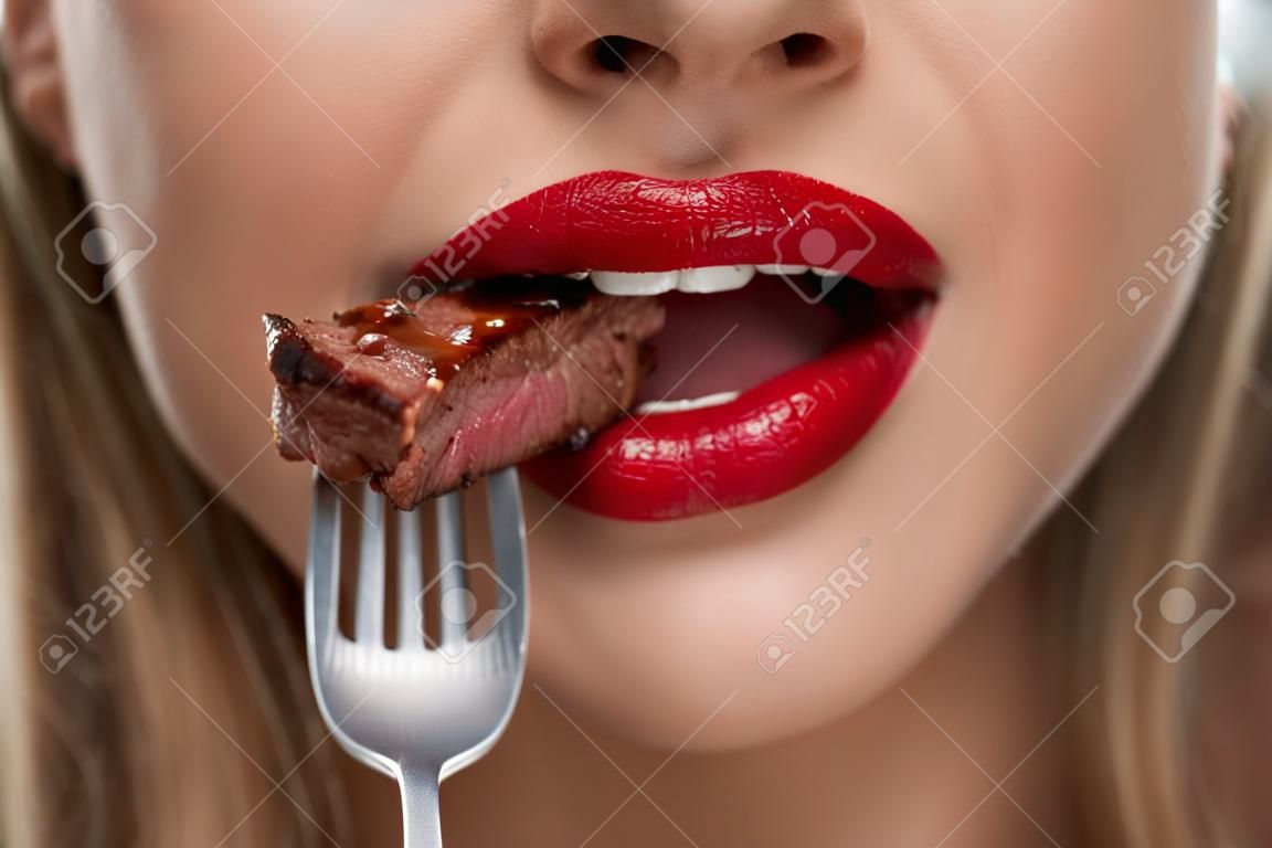 Eating Meat. Closeup Of Woman Mouth With Red Lips, White Teeth Biting Tasty Beef Steak On Fork. Close-up Of Beautiful Female Mouth Eating Delicious Grilled Meat. Nutrition Concept. High Resolution