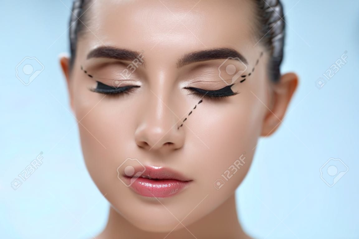 Plastic Surgery Operation. Closeup Beautiful Young Woman Face With Fresh Skin And Perfect Makeup On White Background. Female Face With Black Surgical Lines On Eyelids And Under Eyes. High Resolution