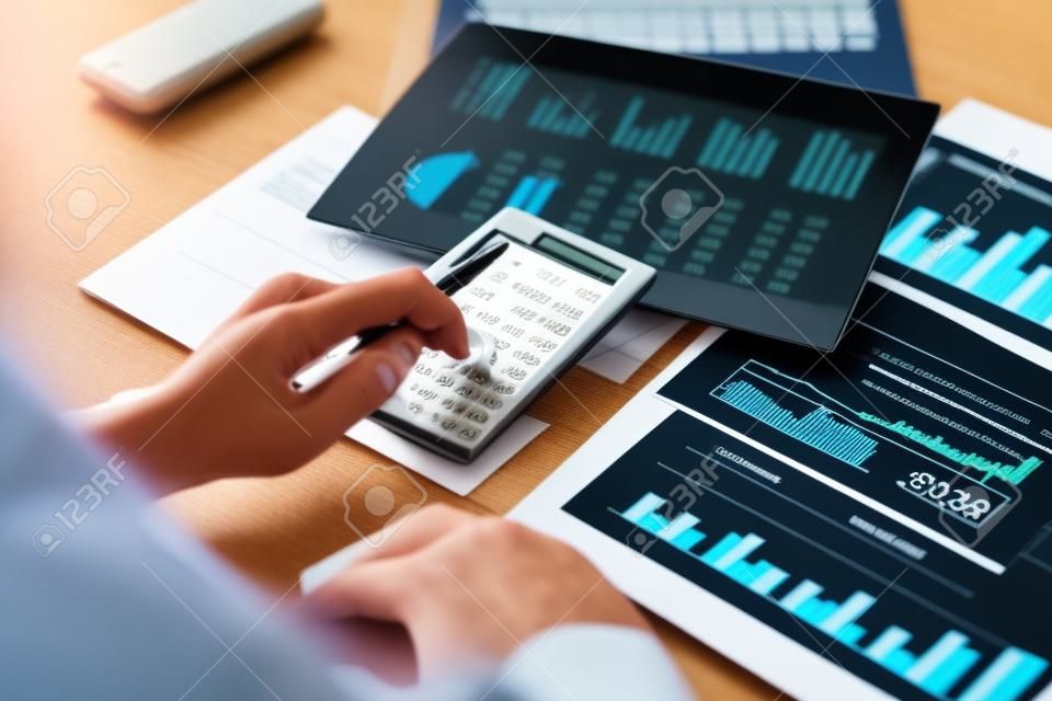 Os empresários de contabilidade estão calculando o imposto de renda da empresa com calculadoras e gráficos sobre as mesas, conceito de análise de lucro financeiro e bancário.