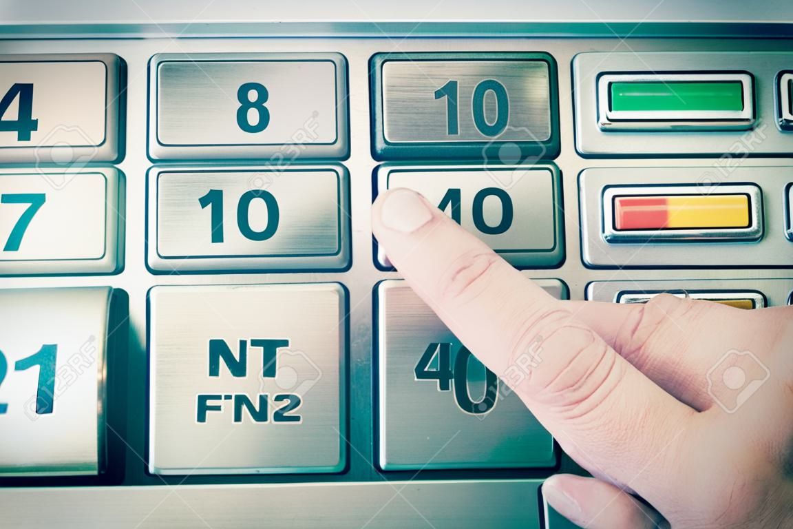 Primer plano de un dedo presionando el botón en cajero automático con el color del teclado metálico tonificado