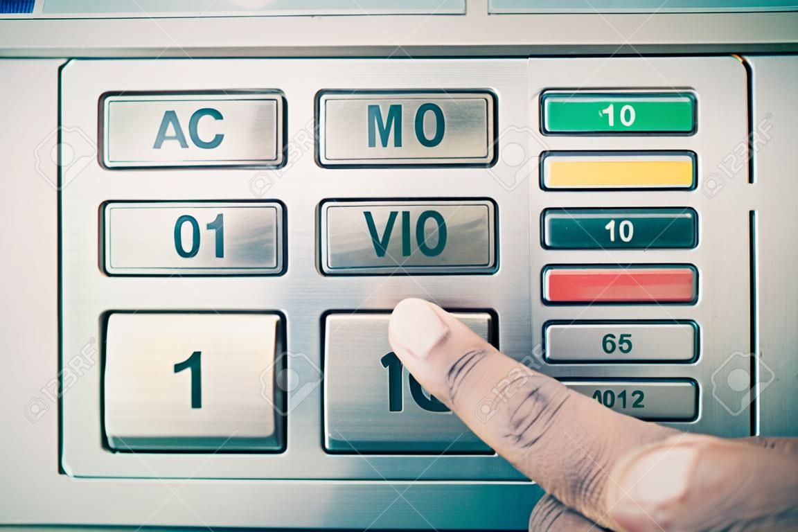 Primer plano de un dedo presionando el botón en cajero automático con el color del teclado metálico tonificado