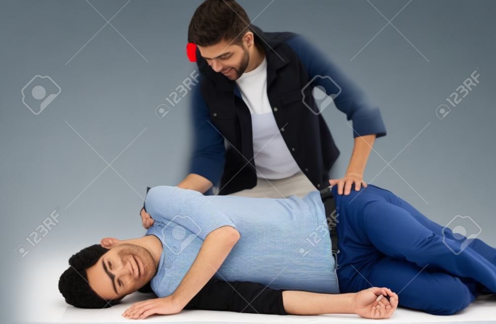 Çift erkek hasta kurtarma pozisyonunda yatarken ve dişi onunla üstünde oturan ilk yardım tekniklerini gösteren.