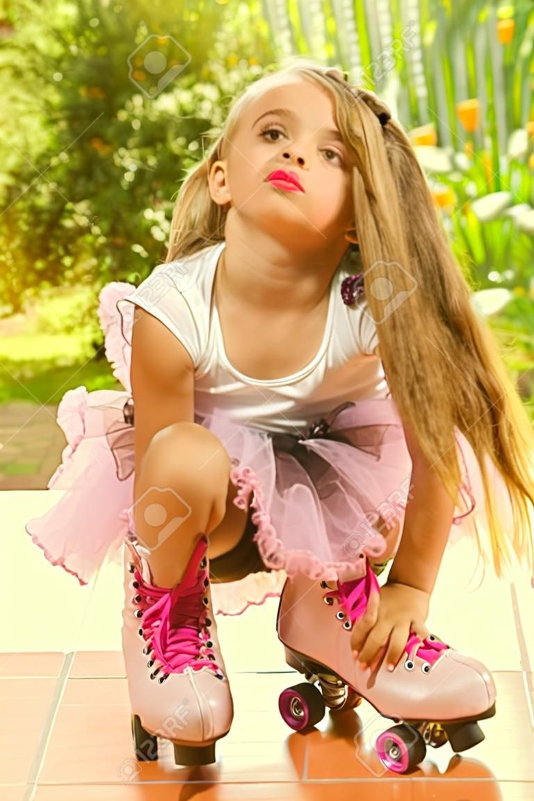 Little girl preschool crouching on ground wearing her roller skates, in a garden background