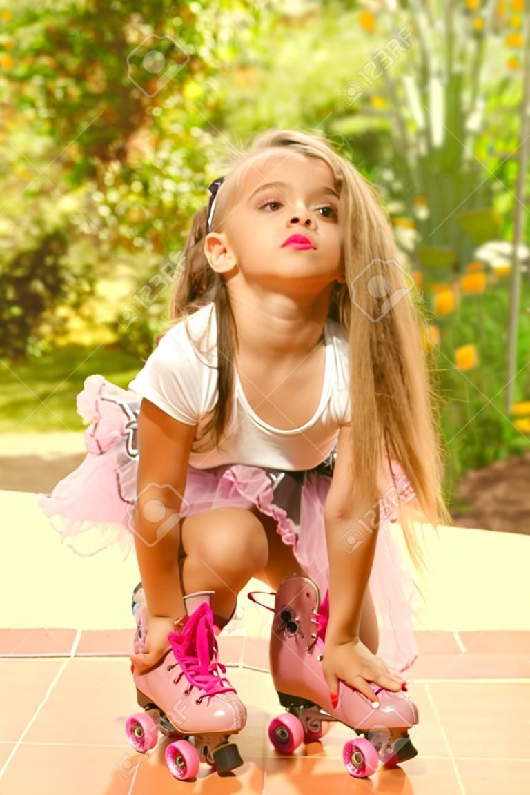 Little girl preschool crouching on ground wearing her roller skates, in a garden background