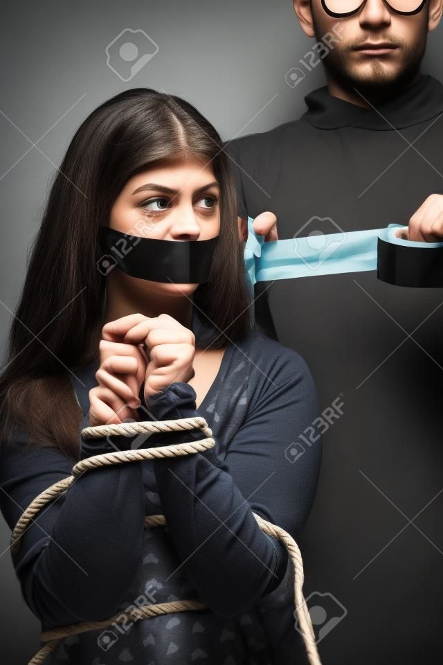 关闭的男人用胶带盖住女人的嘴，用绳子绑住她的手。家庭暴力或绑架的概念