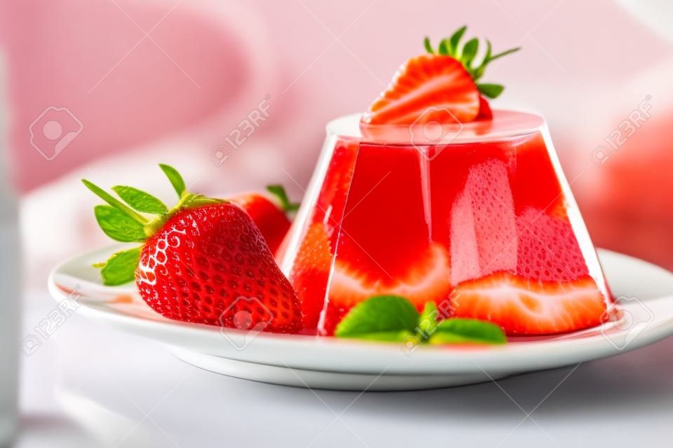 Zdjęcie galaretki owocowej ze świeżą truskawką. Zdrowe jedzenie. Galaretka truskawkowa na białym talerzu. Letni deser z galaretką owocową i świeżą truskawką