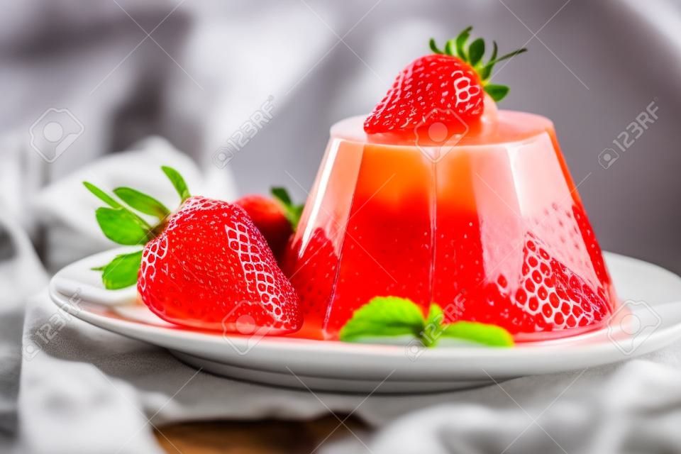 Photo of fruit jelly with fresh strawberry. Healthy food. Strawberry jelly on white plate. Summer dessert with fruit jelly and fresh strawberry