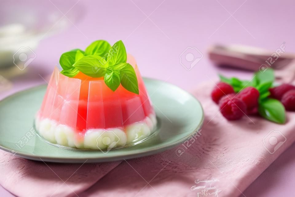 Foto del postre de gelatina de verano con frambuesa. Adornado con una ramita de albahaca fresca sobre fondo claro