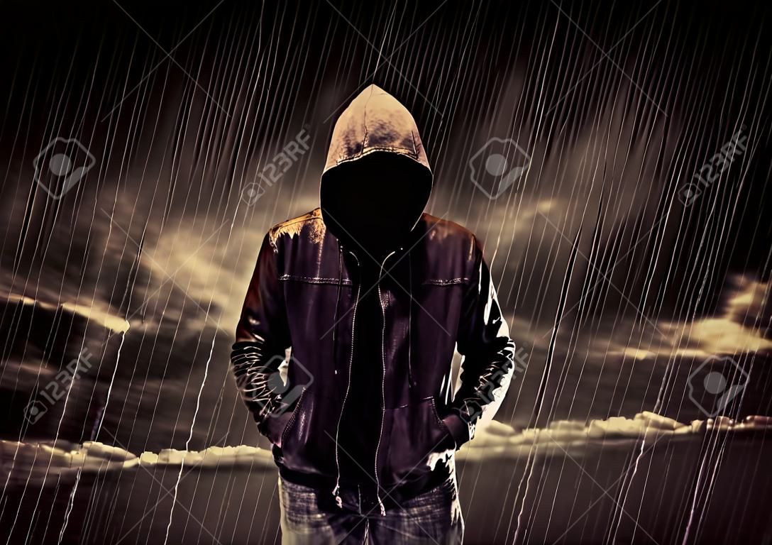 Un voleur sans visage en coton ouaté méconnaissable debout au milieu de la nuit sous la pluie en face du concept de paysage