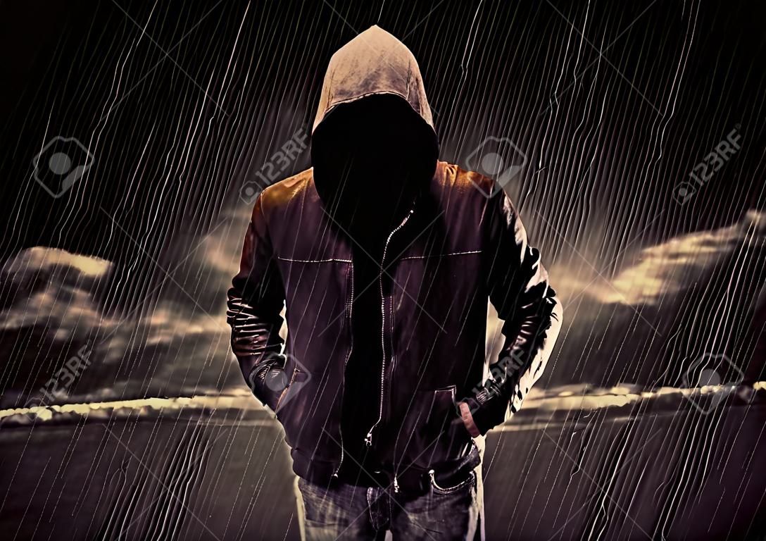 Anonimowa Złodziej w nierozpoznawalne kapturem stojąc w środku nocy, w deszczu przed krajobrazu koncepcji