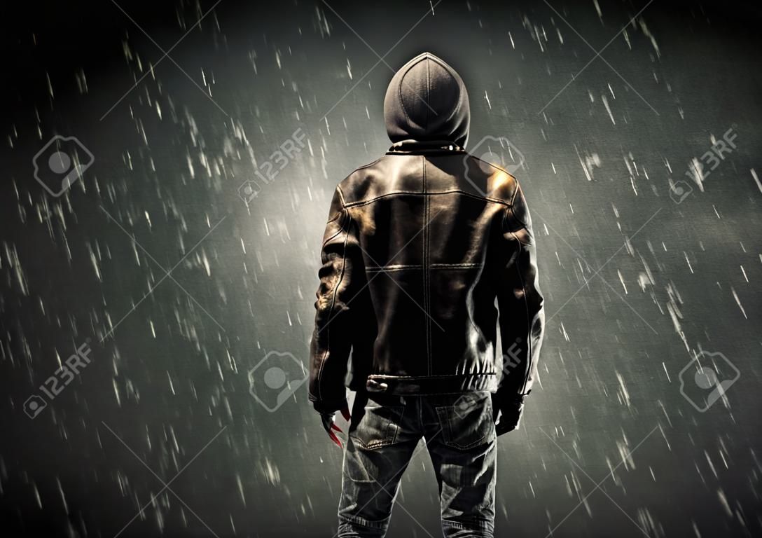 Un uomo misterioso senza volto in hoodie e giacca di pelle in piedi al buio con un concetto di silhouette visibile