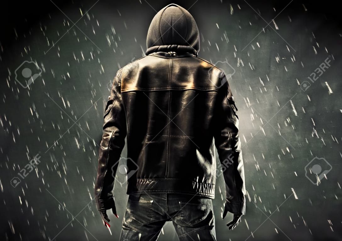 Un uomo misterioso senza volto in hoodie e giacca di pelle in piedi al buio con un concetto di silhouette visibile
